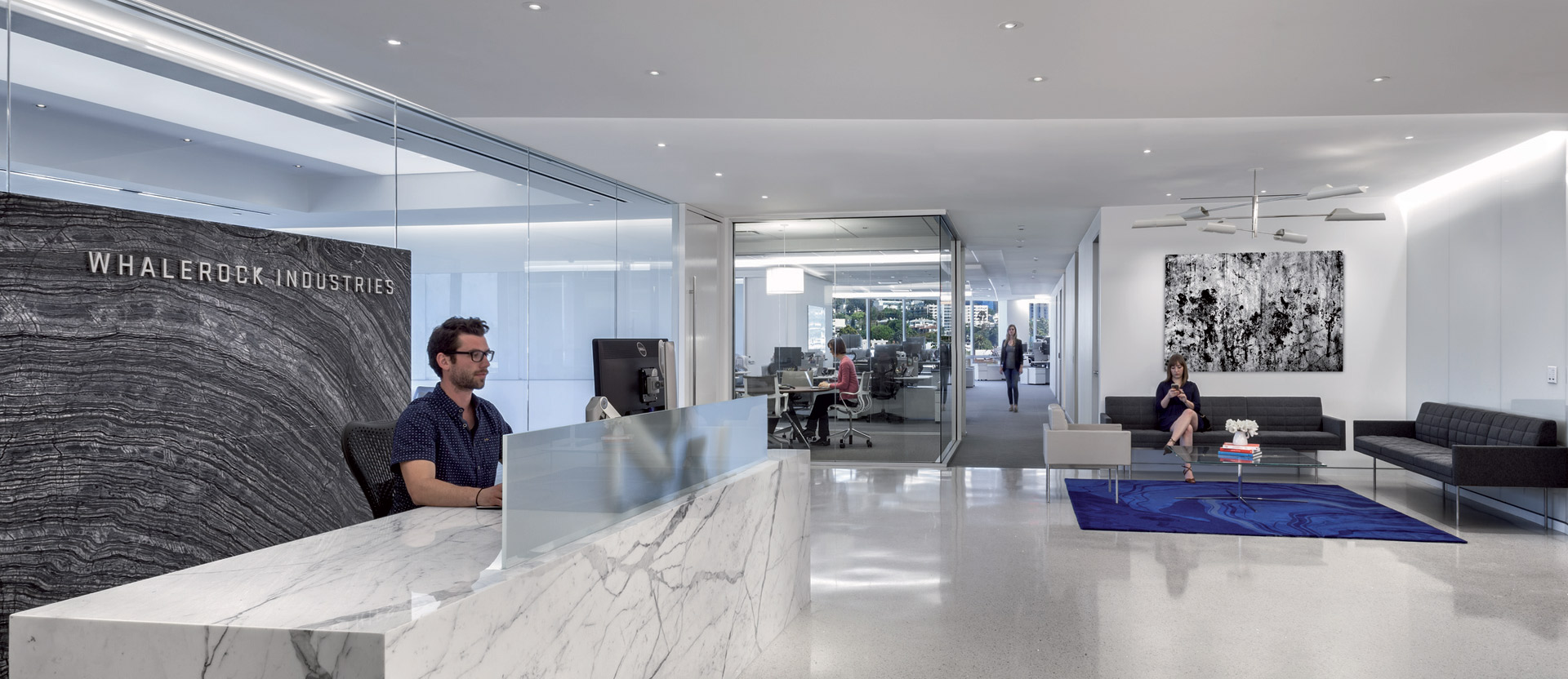 Spacious office lobby with natural light featuring a striking white marble reception desk, minimalist black seating, and modern art. Sleek lines and neutral tones create a welcoming yet professional atmosphere.