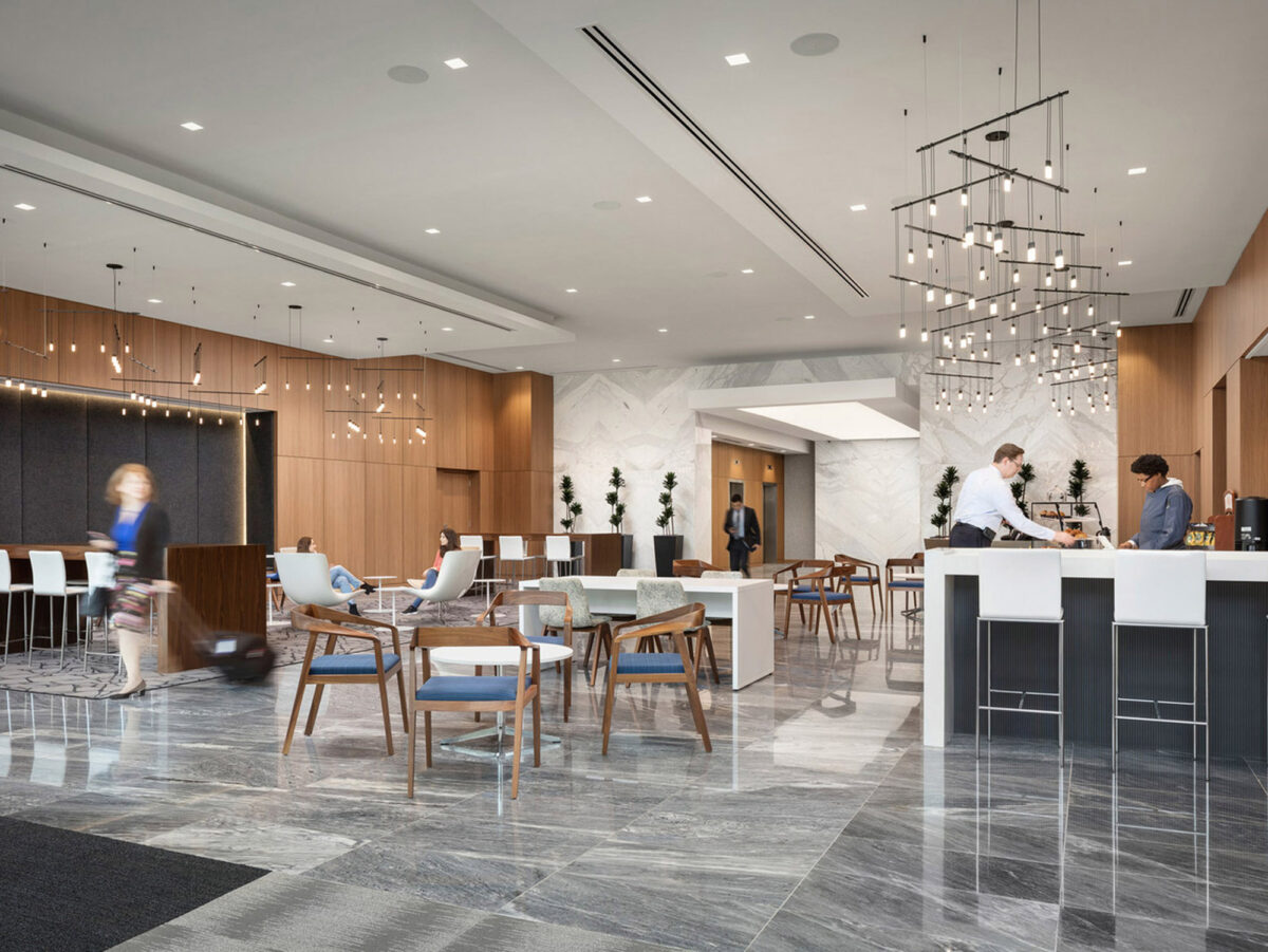 Modern open-plan lobby featuring a neutral color palette with wooden wall accents, complemented by geometric floor tiles. A suspended, artistic lighting fixture draws the eye upward, while mid-century modern furniture adds a touch of elegance. The space balances functionality with aesthetics, capturing an inviting ambiance.