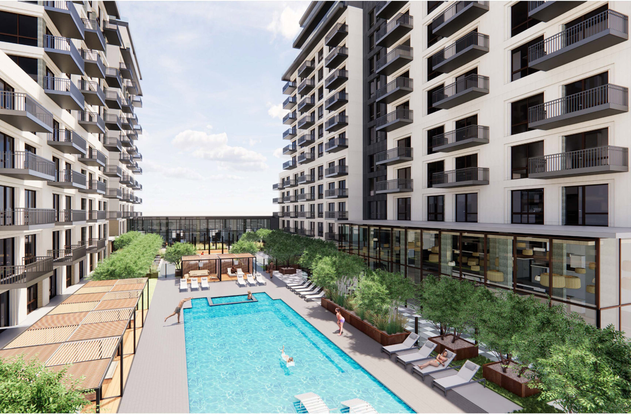 Modern apartment complex with south-facing pool area flanked by symmetrical buildings. Wooden deck with lounge chairs, greenery, and communal spaces promote urban outdoor living. Sunlight enhances the inviting ambiance.