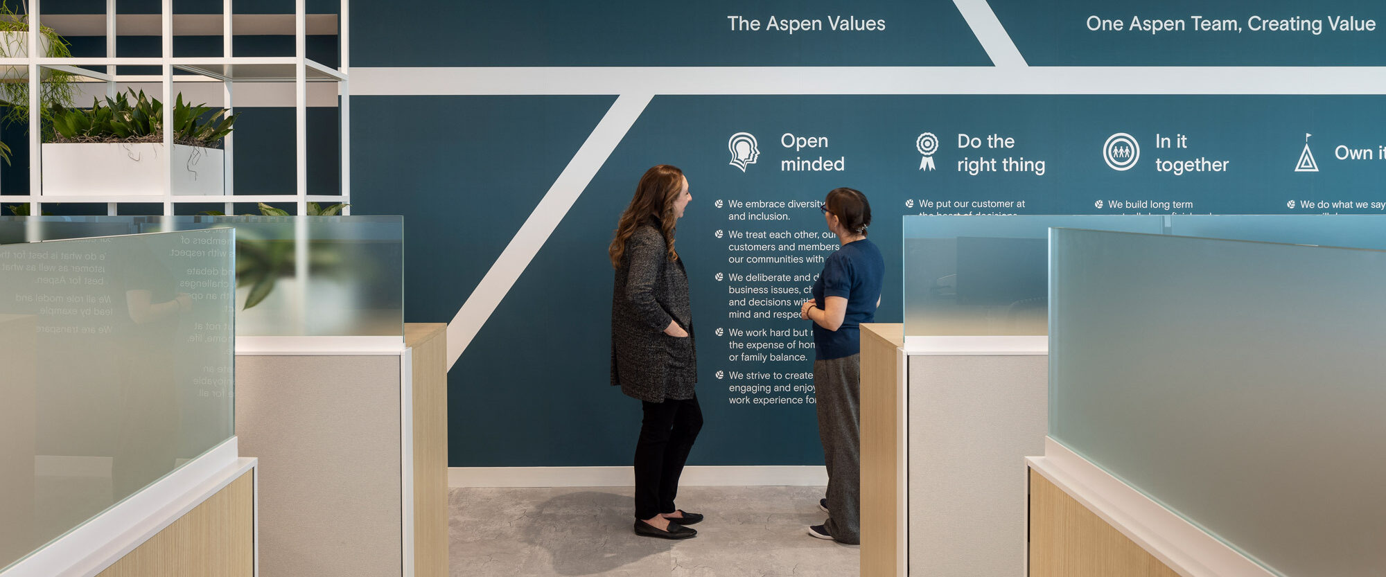 Modern office lobby featuring a geometric patterned accent wall with the company’s core values displayed, fostering a collaborative atmosphere as two professionals engage in conversation.