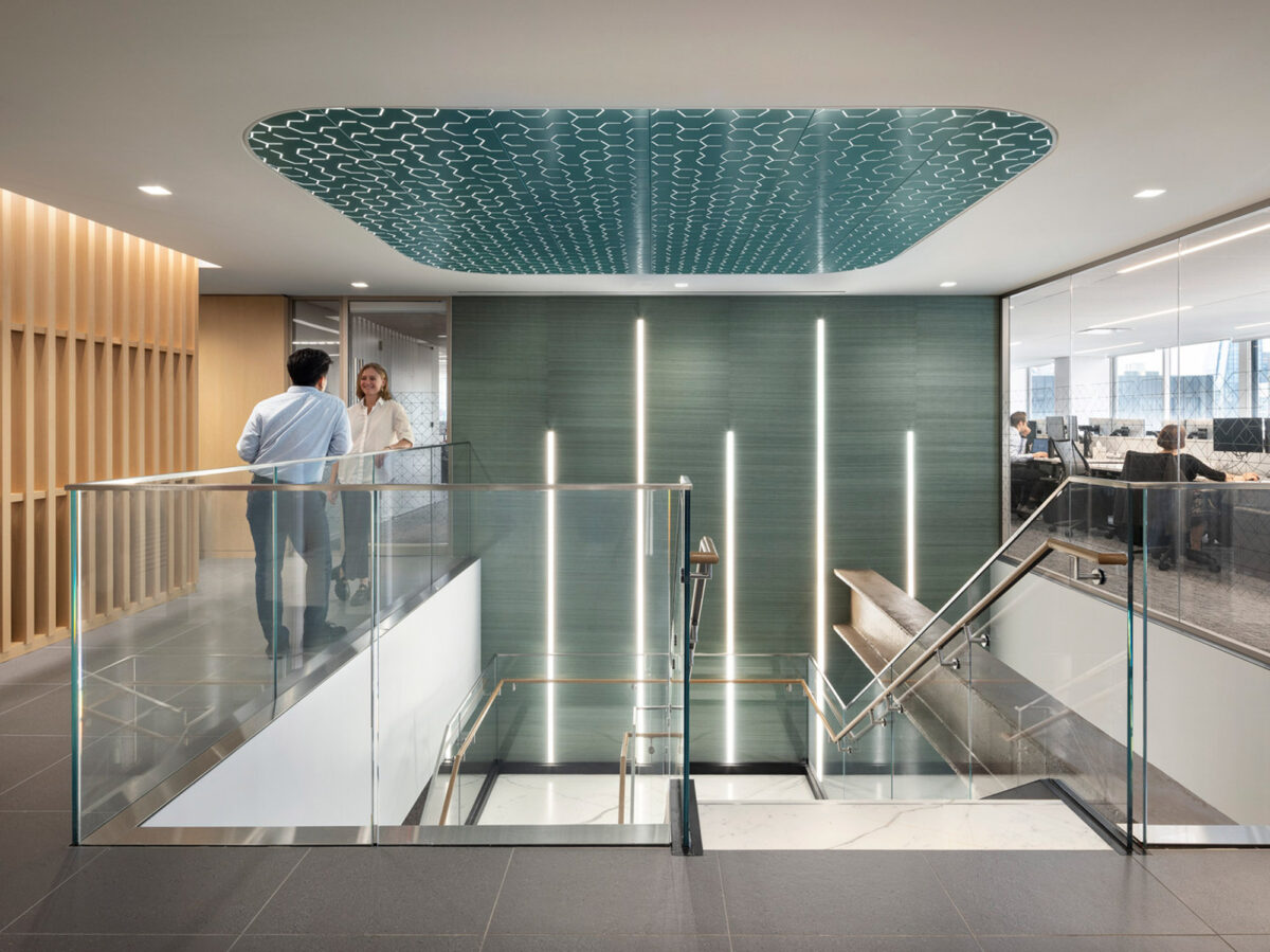 Modern office lobby with an organic wave-patterned ceiling feature, backlit glass partition walls, and warm wooden panel accents complementing the sleek glass balustrades of the central staircase.
