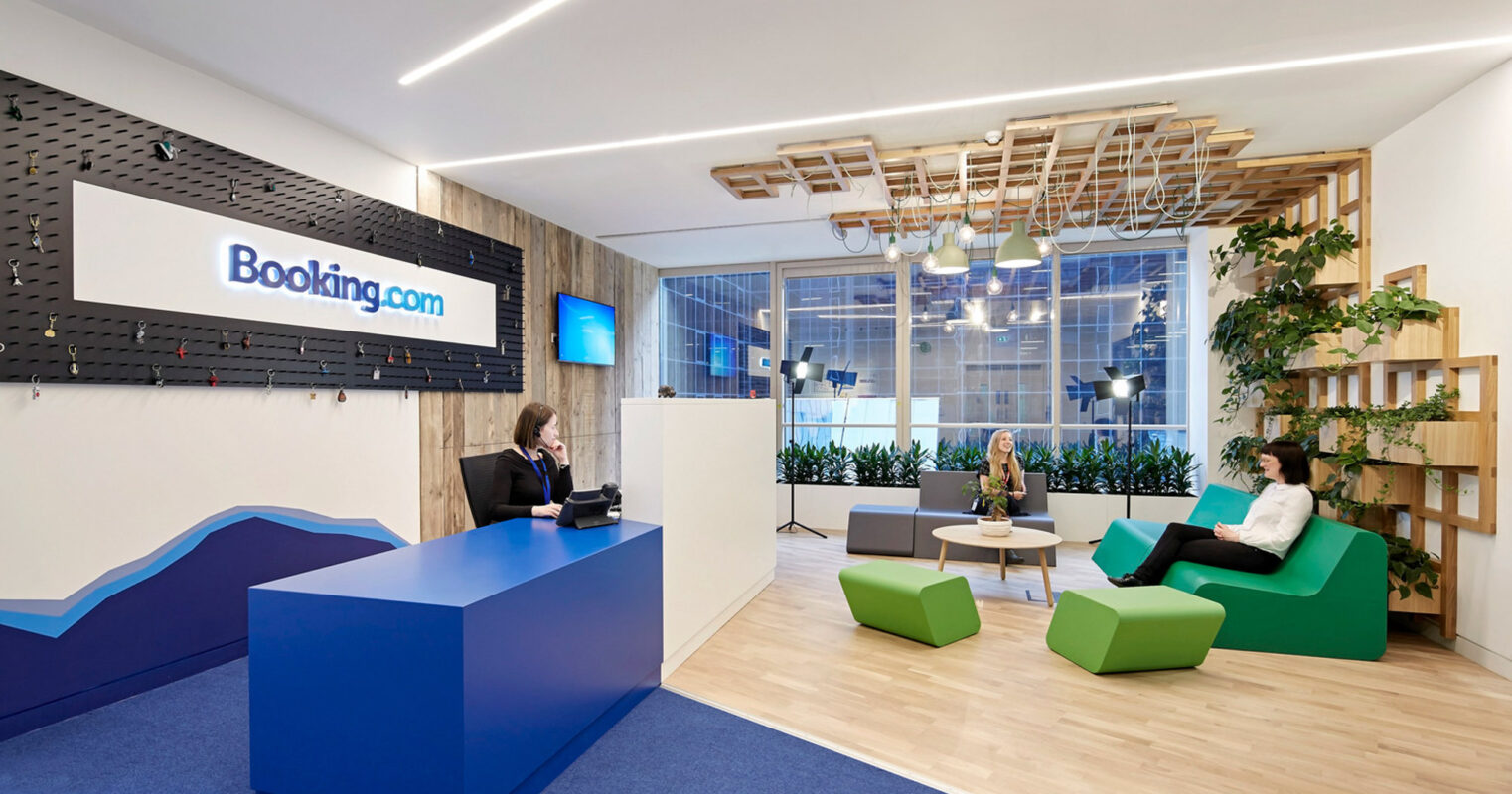 Bright, modern office reception area with a contemporary design featuring an illuminated logo on textured black wall, angular front desk, wood slat ceiling details, and vibrant green seating accents, fostering a dynamic and welcoming environment.