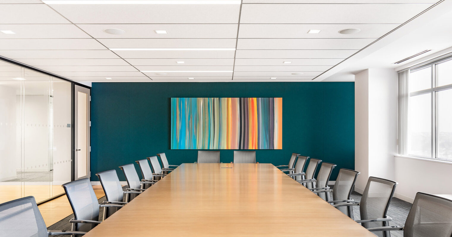 Modern conference room featuring a long, polished wooden table surrounded by sleek, black rolling chairs. A vibrant, striped art piece commands attention against a deep teal accent wall, while the natural light from adjacent windows enhances the room's spacious, clean aesthetic.