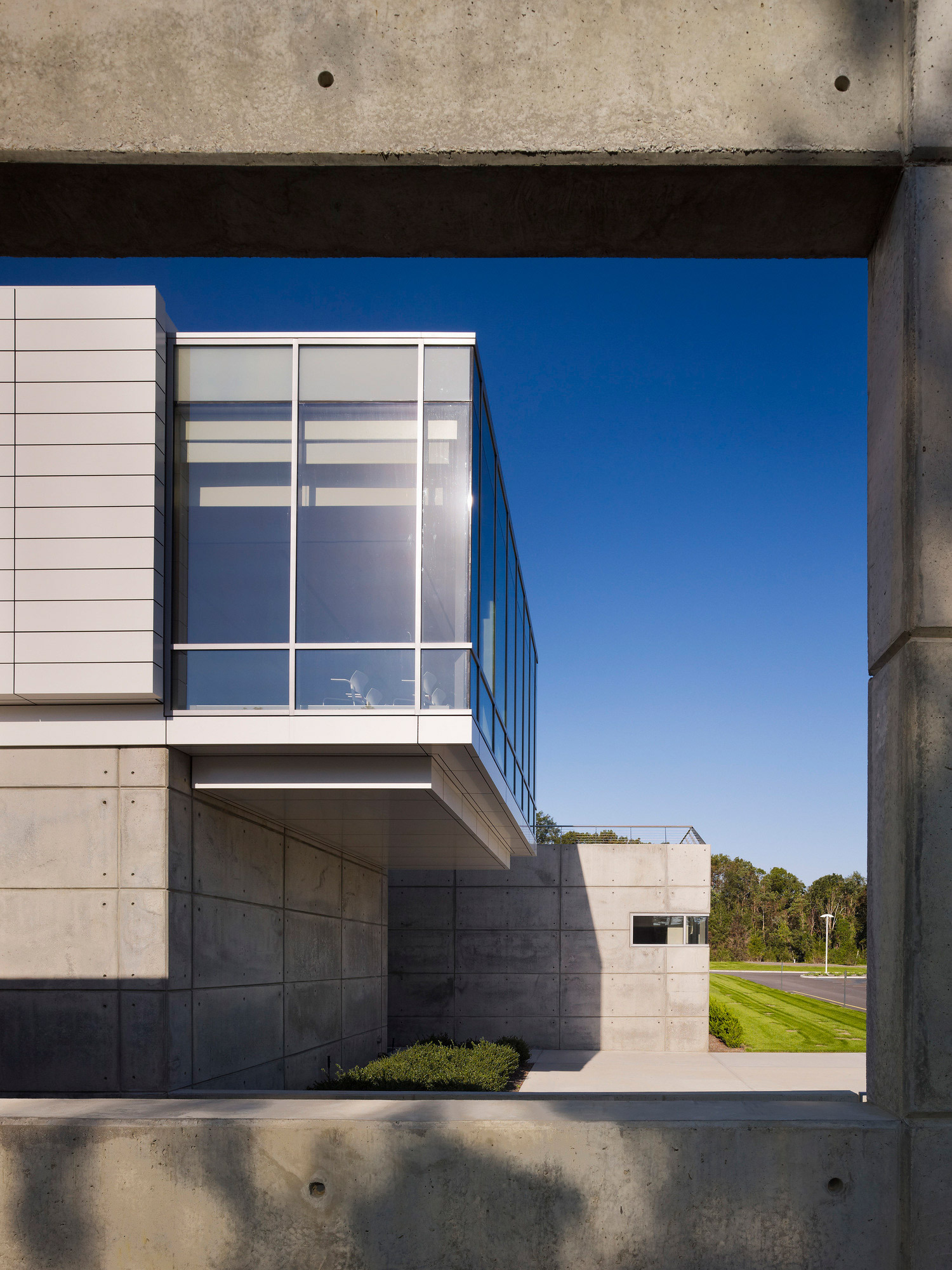 Modern architectural design showcasing a juxtaposition of materials with a prominent concrete frame, a sleek glass facade, and metal paneling complemented by clean lines and a minimalist aesthetic. The overhanging structure creates an inviting outdoor balcony space, reflecting a contemporary approach to form and function.