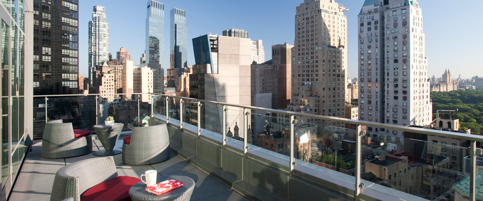 Rooftop terrace with woven outdoor furniture set against a backdrop of New York City's skyline, showcasing modern urban outdoor design integrating cozy seating areas with metropolitan views.