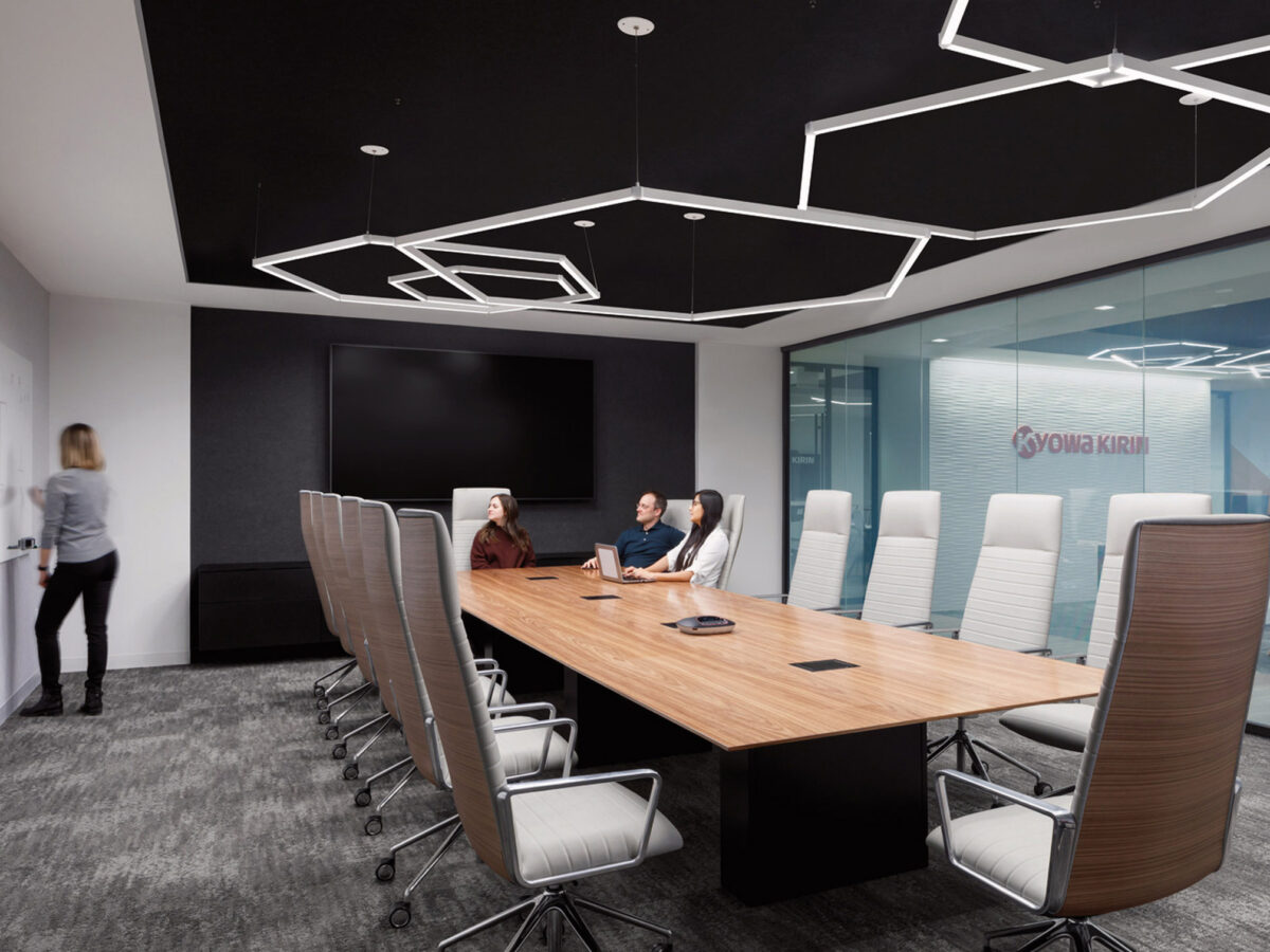 Contemporary boardroom featuring an elongated wooden table with surrounding mesh-back chairs, angular overhead lighting elements, and glass walls providing a glimpse into the adjacent office.