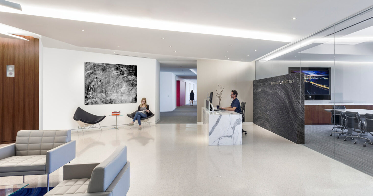 Minimalist reception area with white walls and sleek furniture, featuring a marble reception desk, abstract wall art, and a bold, sculptural chair in monochrome tones, creating a harmonious blend of modern artistry and functional design.