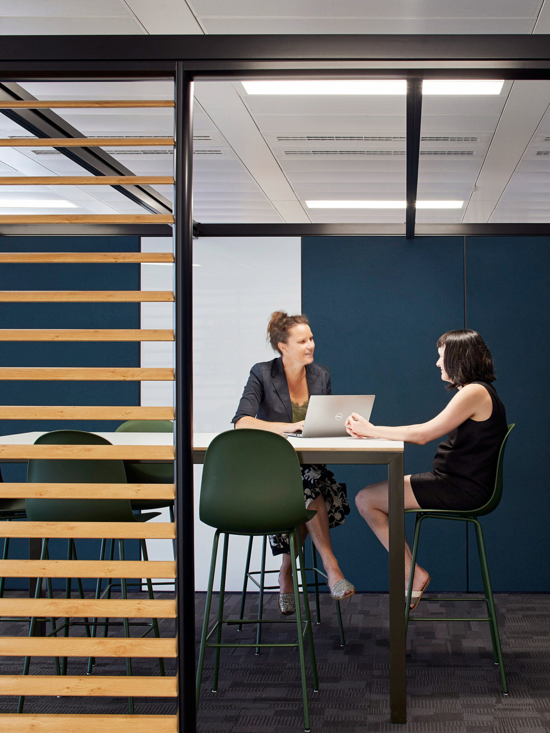 Two professionals converse in a modern office space with glass partitions, highlighting the use of natural light and open design for collaborative workspaces.