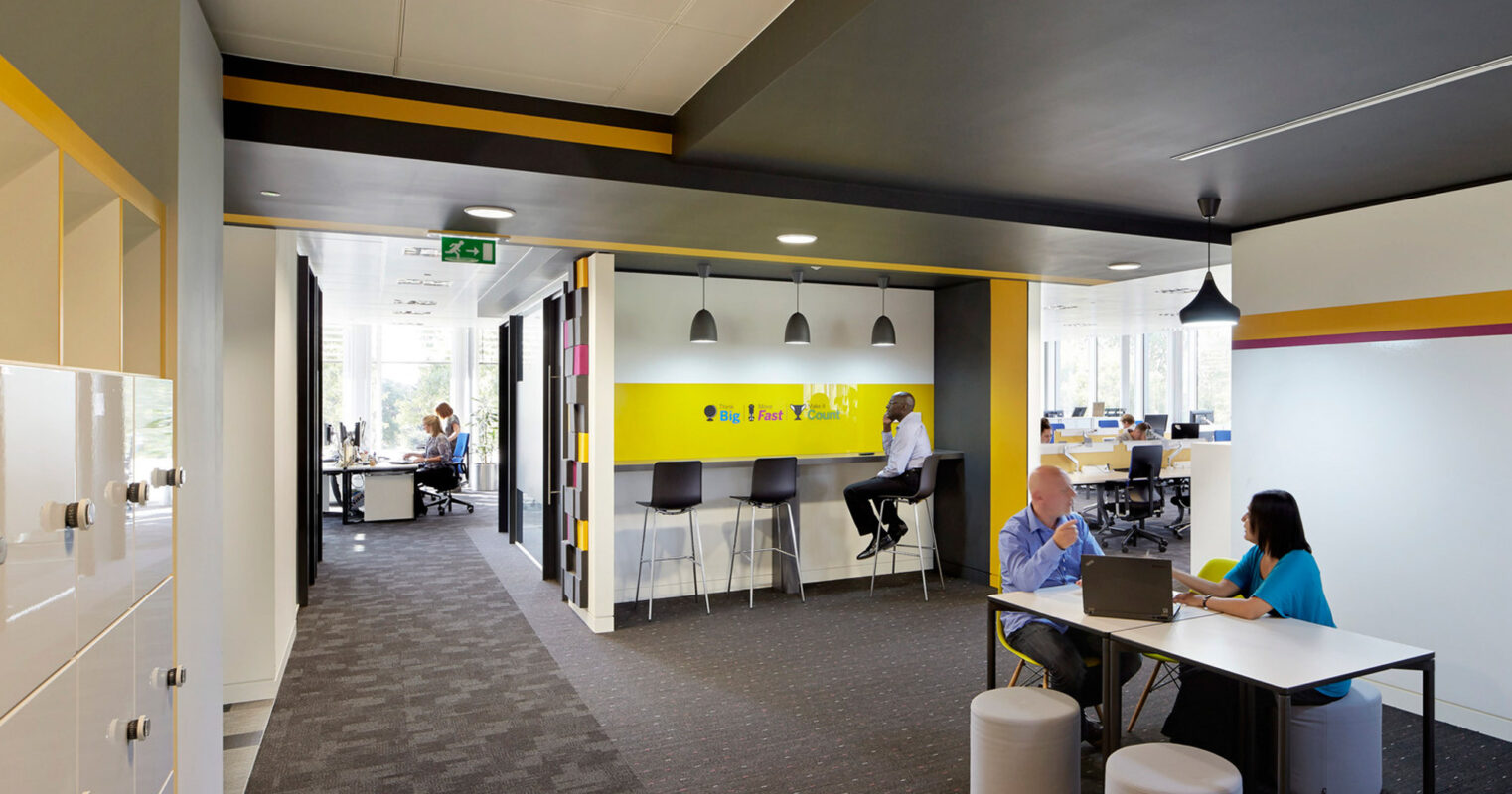 Modern office space with vibrant yellow and white accents, featuring an open layout with glass partitions, ergonomic furniture, and a collaborative work area illuminated by abundant natural light.