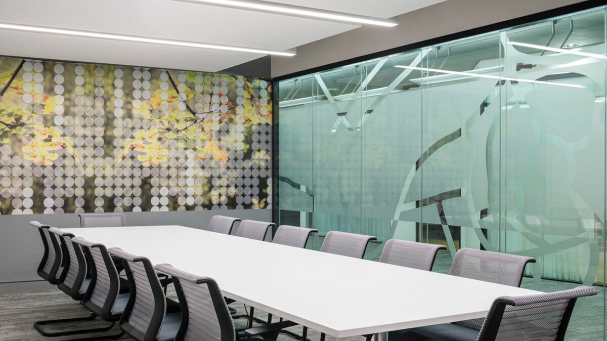Modern conference room featuring an elongated white table with black chairs, complemented by an artistic, floral-patterned accent wall and translucent, frosted glass dividers with etched linear motifs.