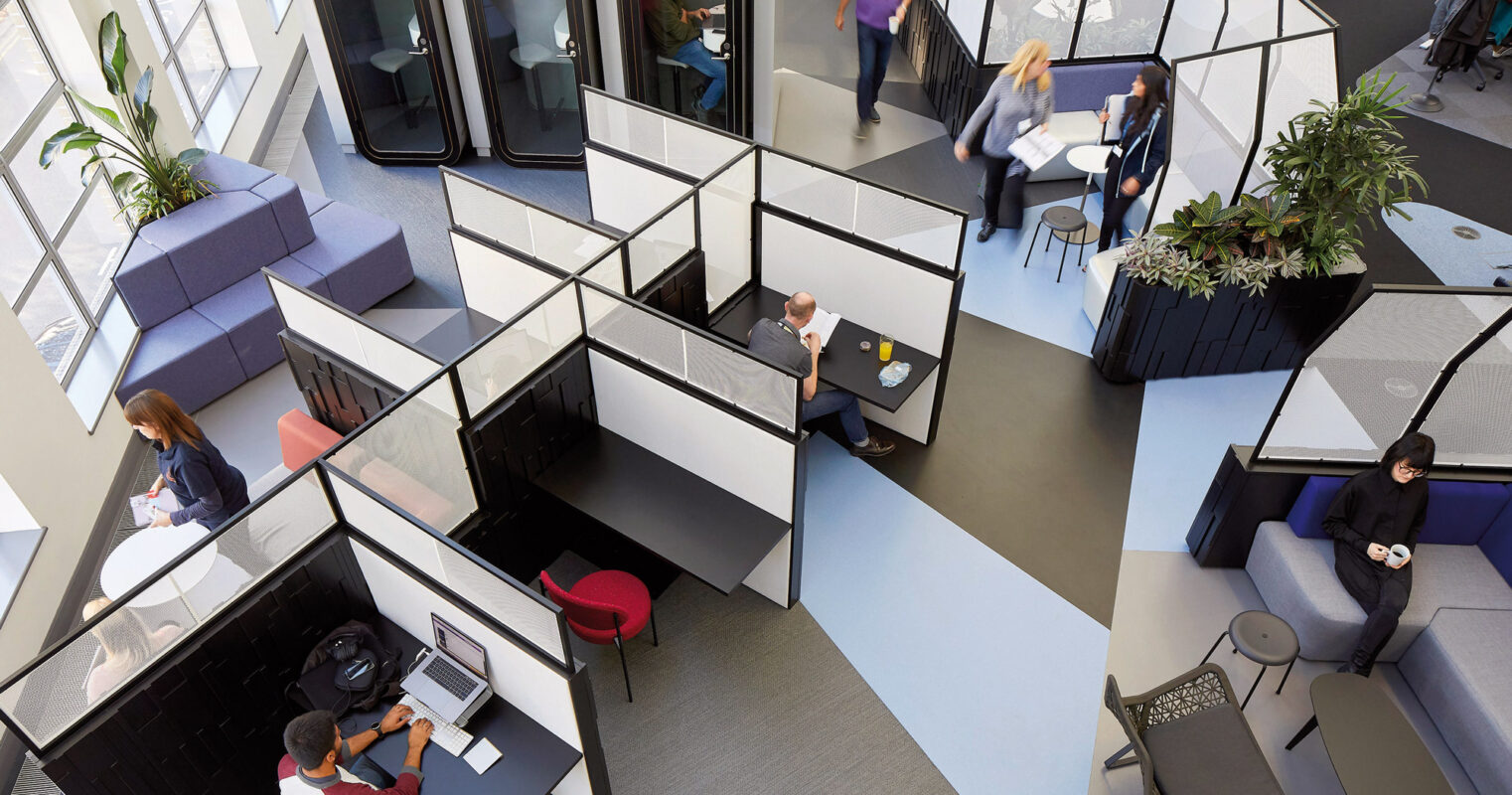 Modern office interior featuring hexagonal pod-like structures for privacy, integrated with open seating areas, and punctuated with indoor greenery to promote a collaborative yet focused work environment. Natural light floods the space, highlighting the geometric forms and the dynamic interaction between communal and personal workspaces.