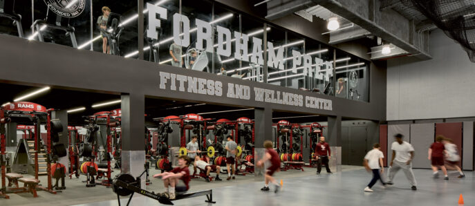 Spacious gym interior with exposed ductwork overhead, reflecting an industrial design. Mirrored walls amplify the space, featuring branded graphics for Fordham University. Red and black gym equipment are organized for functional training, promoting a vibrant, energetic atmosphere.