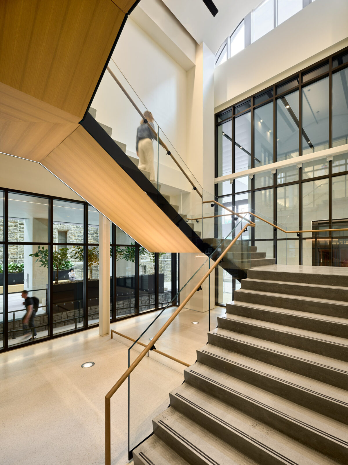 Modern interior showcasing a floating wooden staircase with glass balustrades, enhancing natural light flow from floor-to-ceiling windows, complemented by minimalist design lines and a neutral color palette.