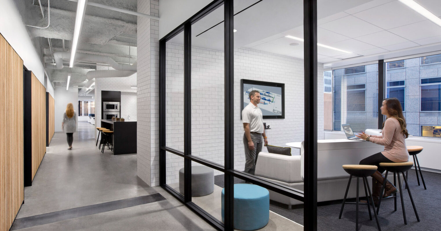 Modern office space showcasing a balance of natural and artificial lighting, with open-concept seating and private glass-walled rooms, juxtaposing exposed concrete ceilings against warm wooden accents and sleek furniture.