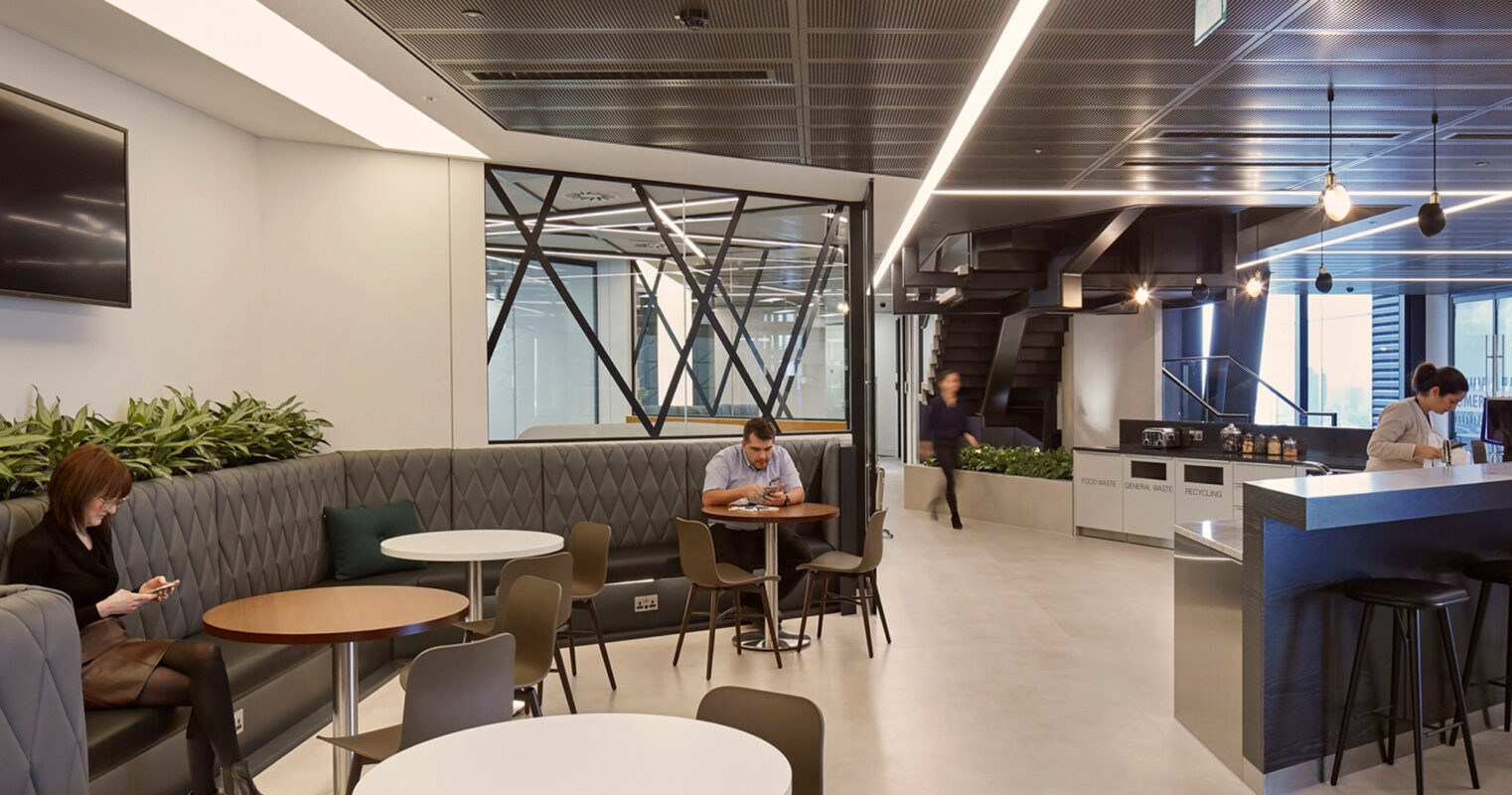 Modern office cafeteria with sleek furniture, pendant lighting, and a monochromatic color scheme, accented by vibrant green upholstery and plant life, creating a contemporary, inviting space for employees.