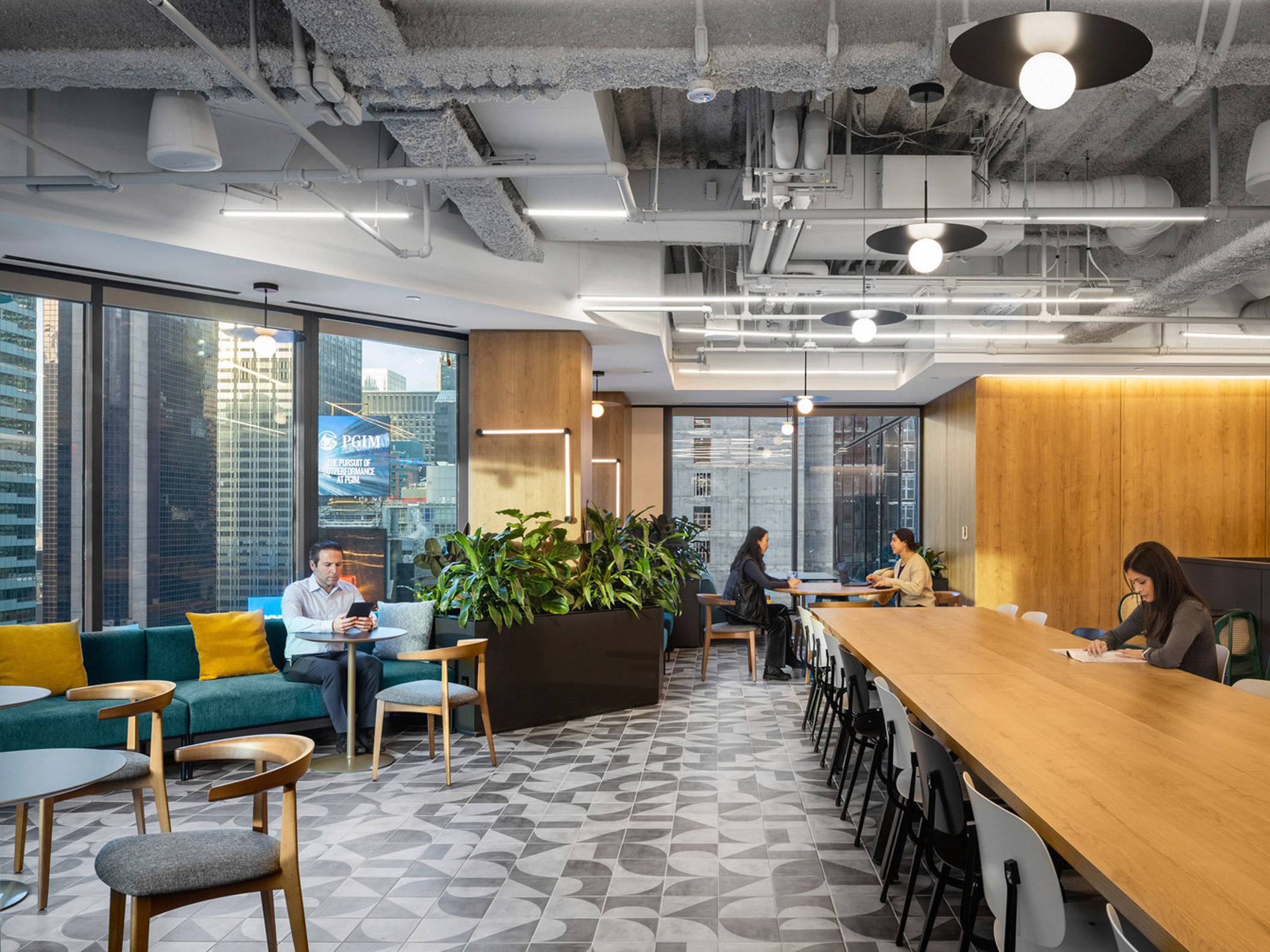 A modern office break room featuring a geometric-patterned floor, various seating options including bar-height tables and plush couches, accented by vibrant furnishings and ample greenery, bordered by floor-to-ceiling windows overlooking an urban landscape.