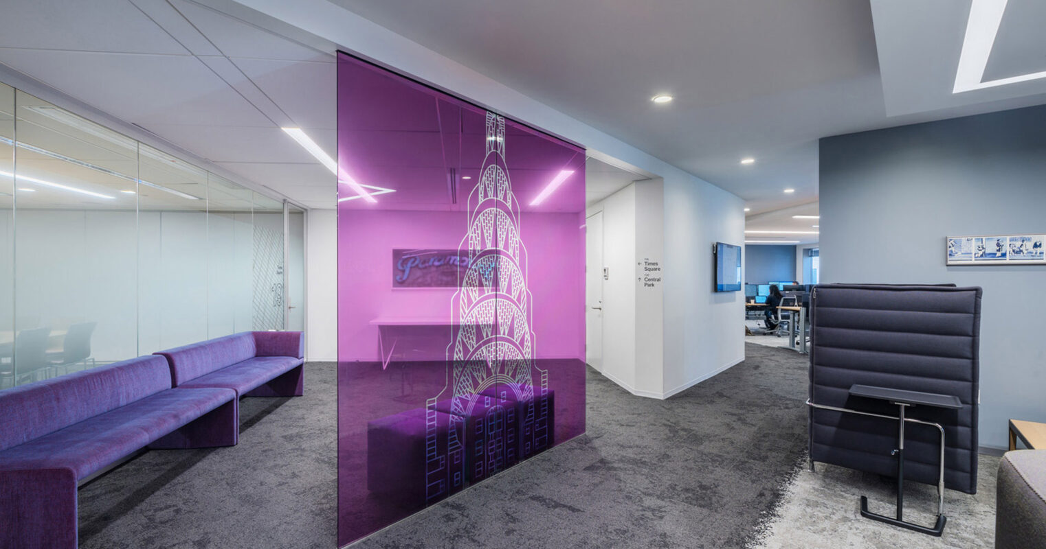 Modern office space with a vibrant, purple glass partition featuring an etched Eiffel Tower design. Sleek gray flooring juxtaposes the plush purple sofas, while white walls and angular light fixtures enhance the contemporary aesthetic.