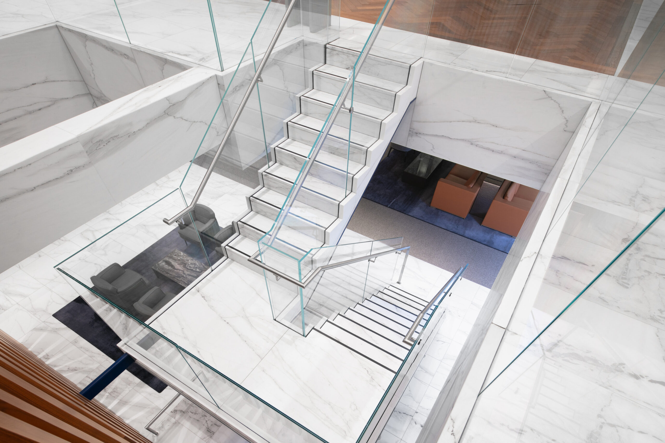 Stunning interior space featuring a contemporary glass staircase that elegantly connects two levels. Polished marble flooring complements minimalist design elements, while a stylish seating area is visible below. Abundant natural light enhances the airy ambiance, creating a seamless flow between spaces and highlighting the modern architectural features.