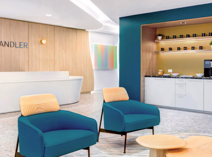 Modern reception area with curved white desk, accented by teal armchairs and wooden stools. A blue alcove with shelving hosts refreshments, set against a warm wooden backdrop with the company’s signage. Ambient lighting complements the room's clean, inviting aesthetic.