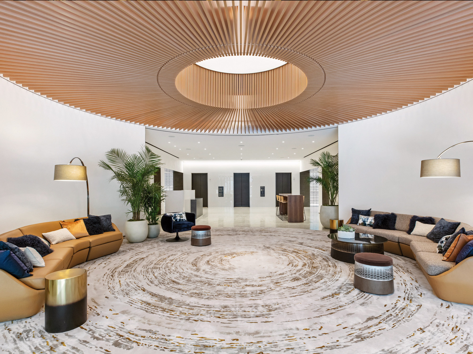 Elegant modern lobby with circular patterned marble floor, wooden slatted ceiling design, and sleek, comfortable seating area complemented by lush indoor plants.