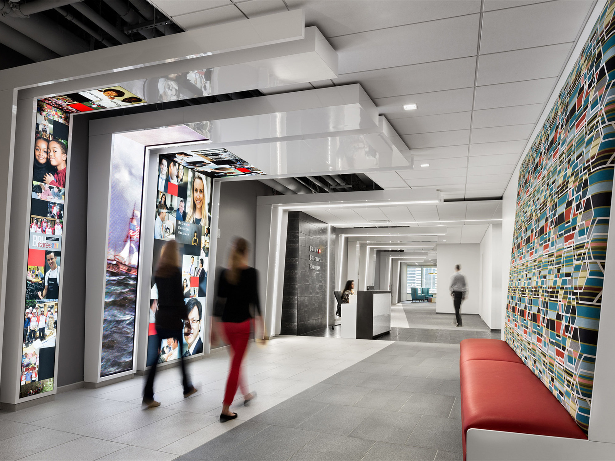 Dynamic office corridor with a mosaic of colorful abstract graphics on one wall, interactive digital displays, a sleek reception area, and modern furnishings, punctuated by the movement of professionals in a fast-paced environment.