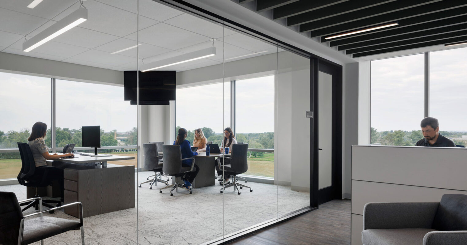 Modern office space featuring a clean, minimalist design with sleek furniture, pendant lighting, and large windows offering ample natural light. Glass walls provide transparency and encourage an open, collaborative environment.