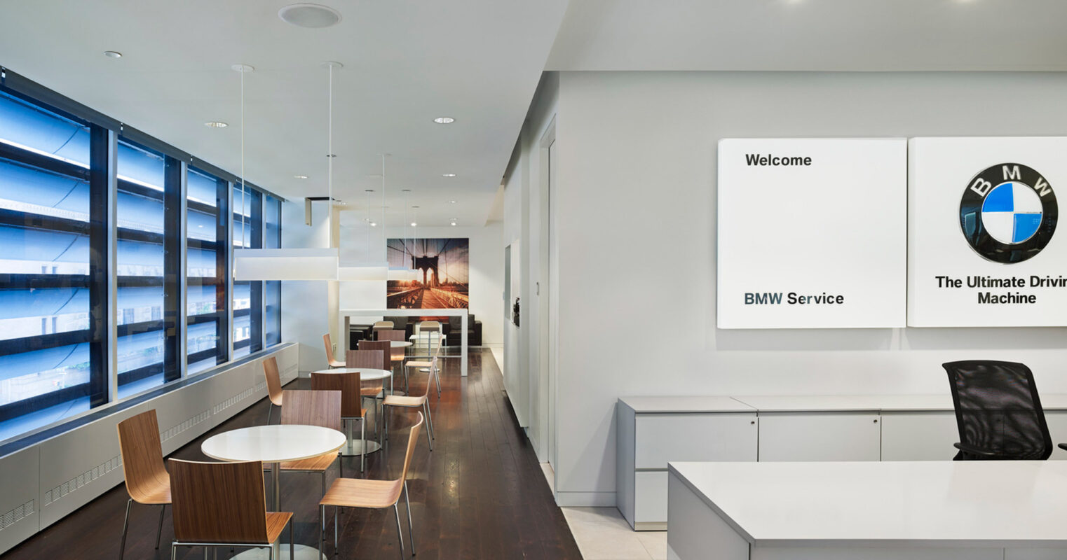 Clean and modern car dealership customer waiting area with seating, large windows, and BMW branding on the wall.