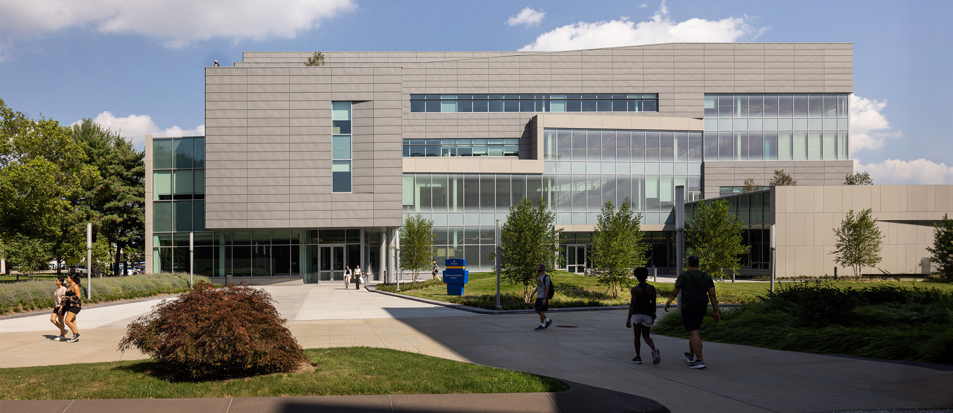 Modern educational building featuring clean lines, expansive glass facade for natural lighting, and aluminum composite panels. Landscaped with young trees and pedestrian pathways, the design encourages student engagement and environmental harmony.