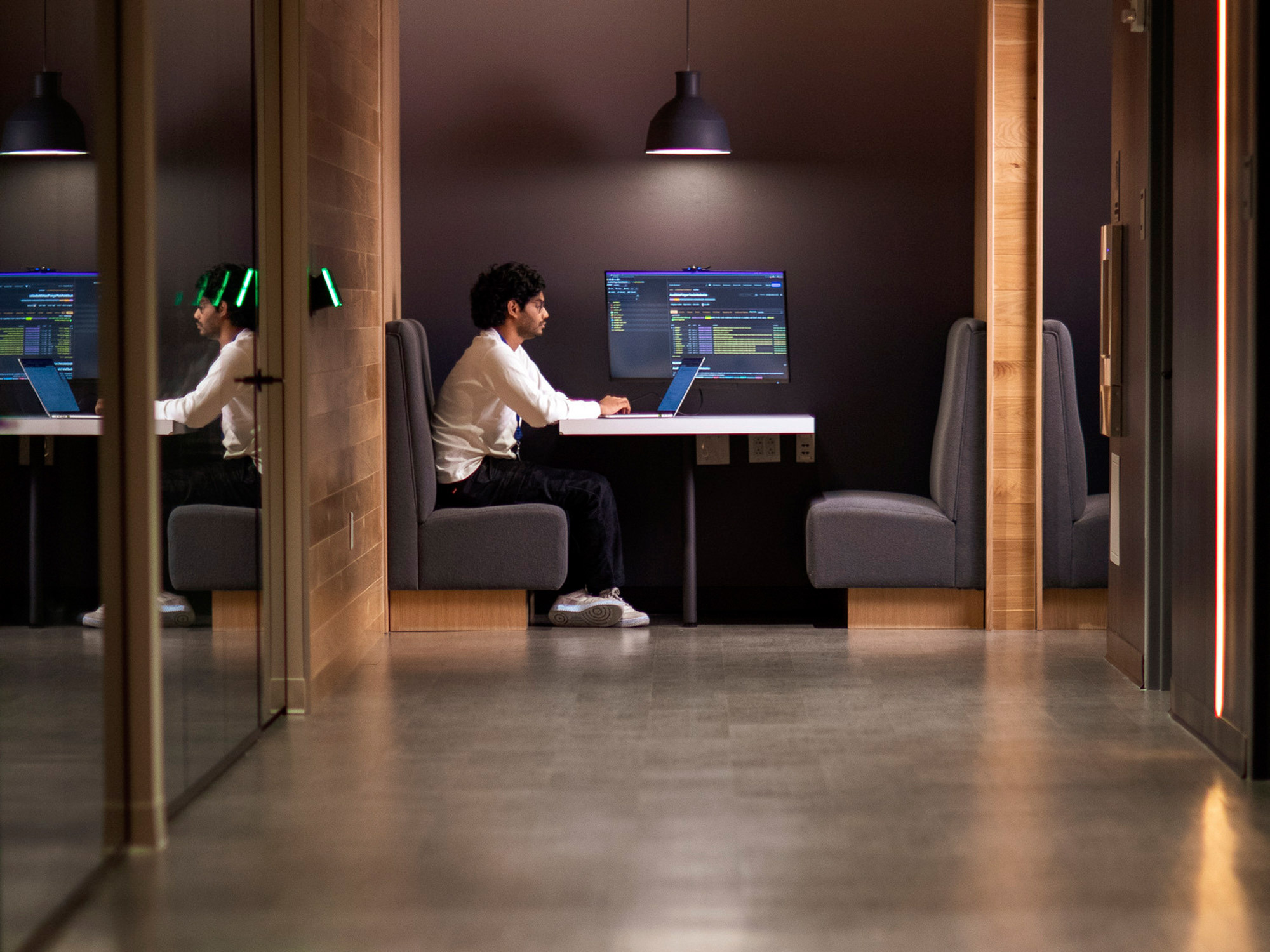 A dimly lit focus area in an office setting with high-backed booths providing privacy for individuals working on computers, creating an ambiance of concentrated productivity.