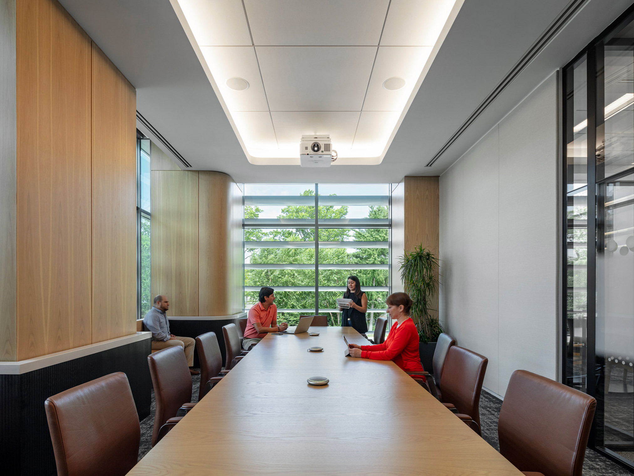 Modern conference room with natural wood paneling, ambient lighting, a sleek rectangular table, and ergonomic chairs. Equipped with audio-visual technology for presentations, the space balances function and style, fostering a collaborative working environment.