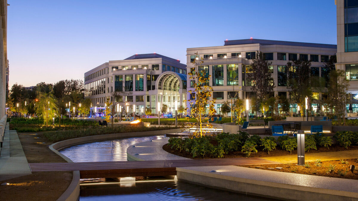 Twilight view of an urban office building featuring neoclassical elements such as a grand arched entrance and symmetrical fenestration, complemented by serene landscaping and a curved reflective water feature forefront.