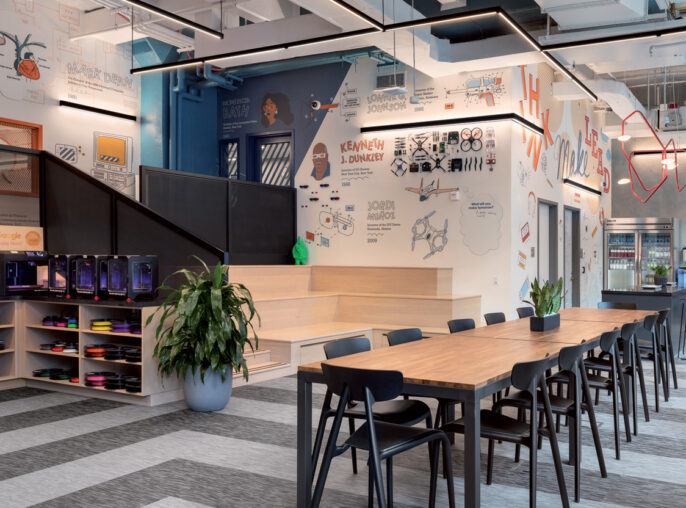 Modern open-plan office with vibrant graphics adorning the walls, featuring a communal wooden table, sleek metal chairs, and ample shelf space with colorful storage units; natural light enhances the room's urban loft aesthetic.