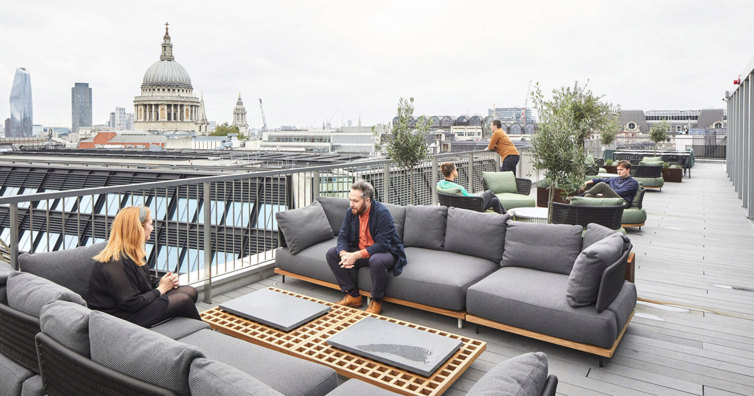 Rooftop garden terrace featuring contemporary, modular lounging furniture with plush cushions, complemented by minimalistic outdoor rugs and wooden accent tables. Urban skyline backdrop includes the iconic dome of St. Paul's Cathedral, enhancing the sophisticated, metropolitan ambiance of the space.