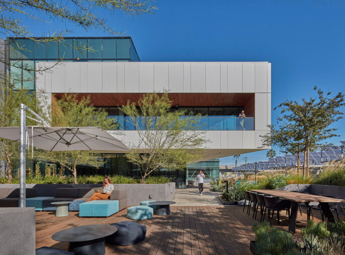 Modern architecture featuring a cantilevered building with clean white facades, expansive glass windows, and an integrated outdoor seating area with contemporary landscaping and hardscaping elements.