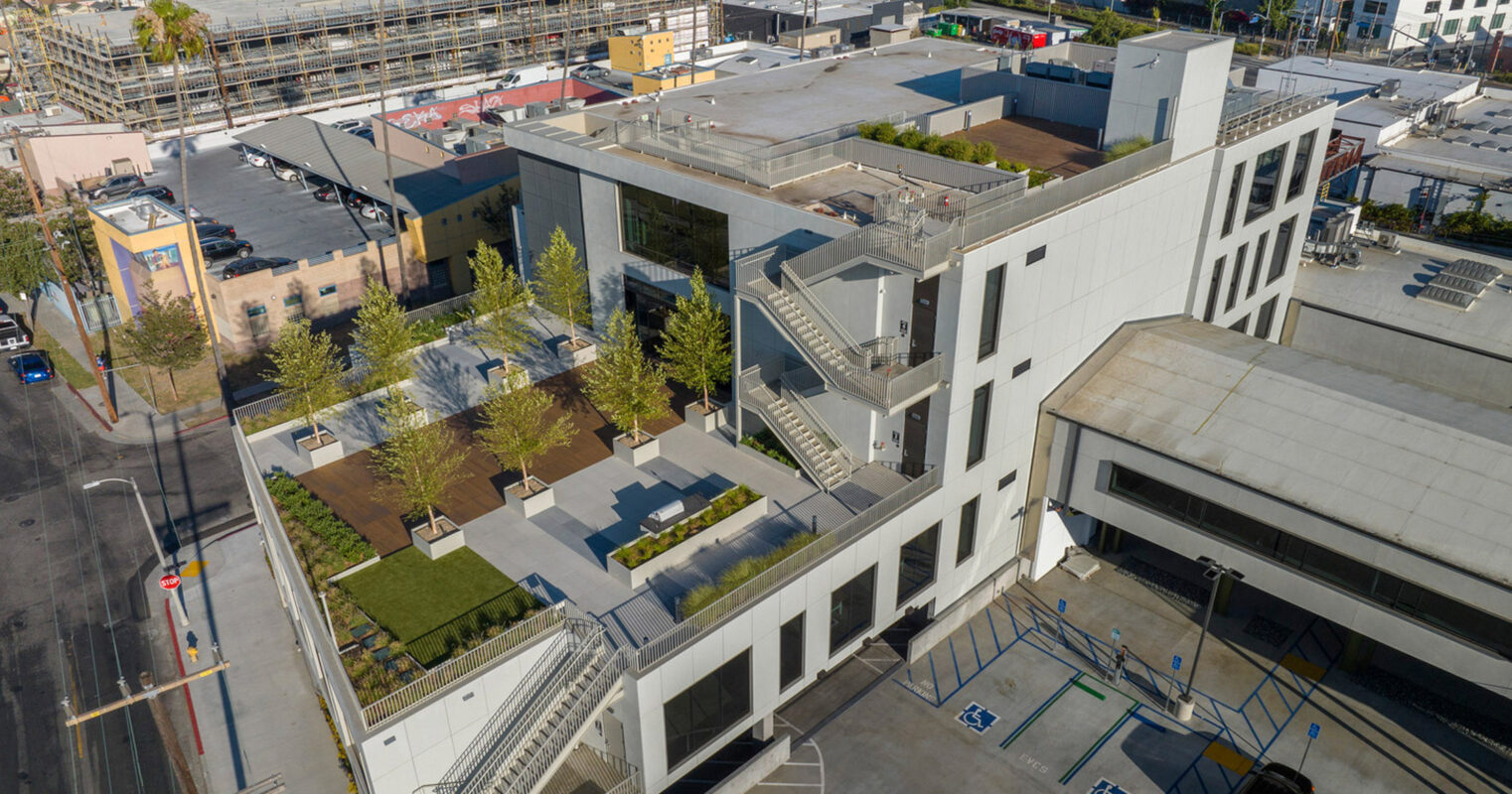 Modern urban building complex viewed from above, featuring geometric architectural design with a rooftop garden, expansive windows, and tiered terraces that promote a blend of indoor-outdoor space.