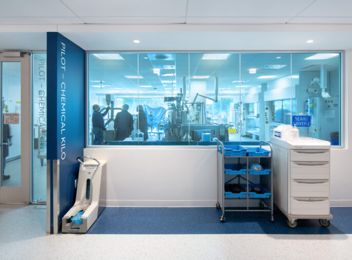 Modern laboratory interior featuring a bright, open design with large glass windows. The space showcases advanced equipment and a streamlined layout, emphasizing functionality and collaboration. A mobile cart with storage bins stands in the foreground, alongside modern lighting that enhances the sterile atmosphere.