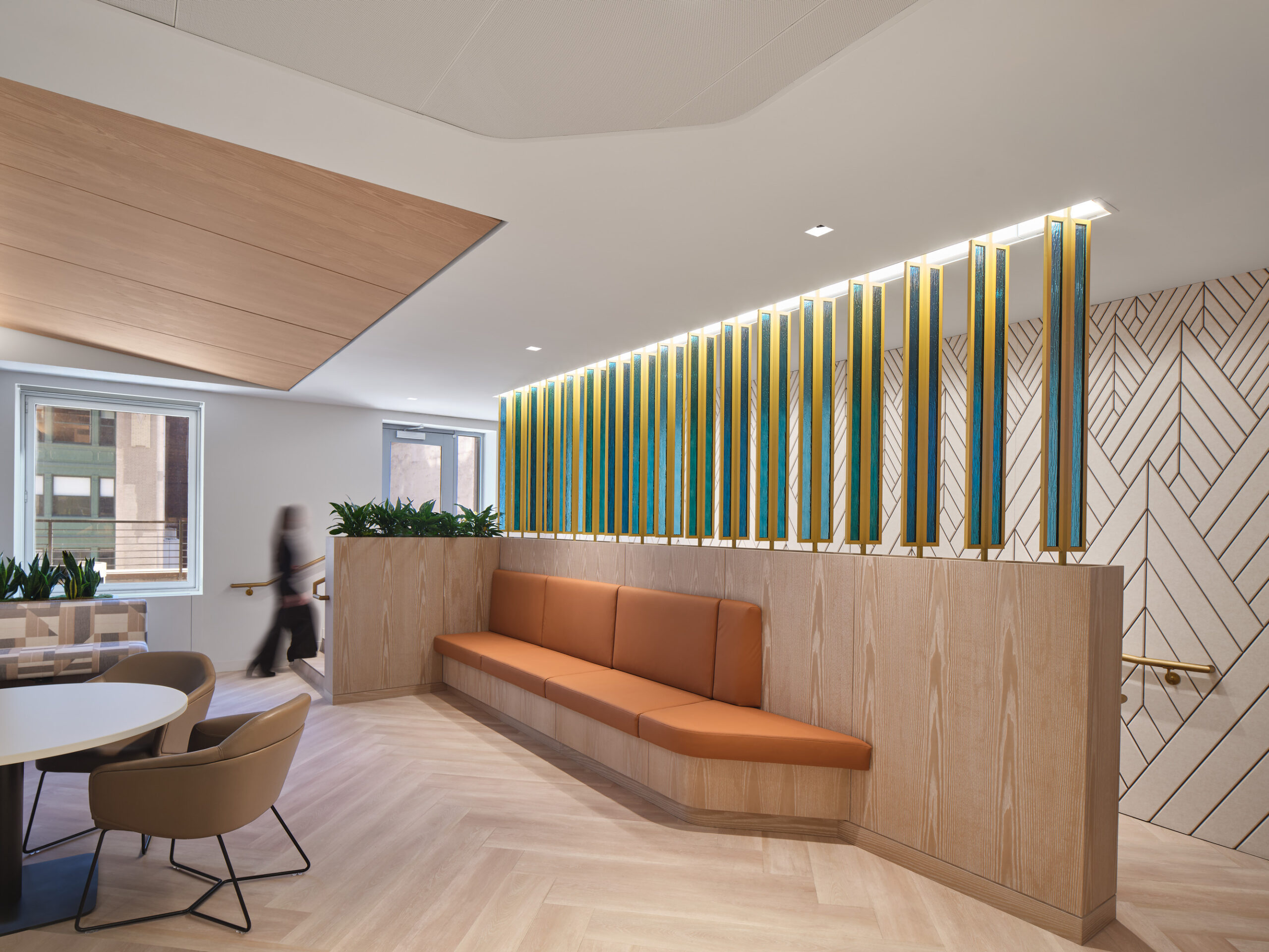 A modern interior design featuring a sleek lounge area with an orange bench against a wood-paneled wall. Vertical blue and yellow accent panels create a striking backdrop, complemented by lush greenery. The space showcases a harmonious blend of textures and colors, enhancing the contemporary aesthetic.