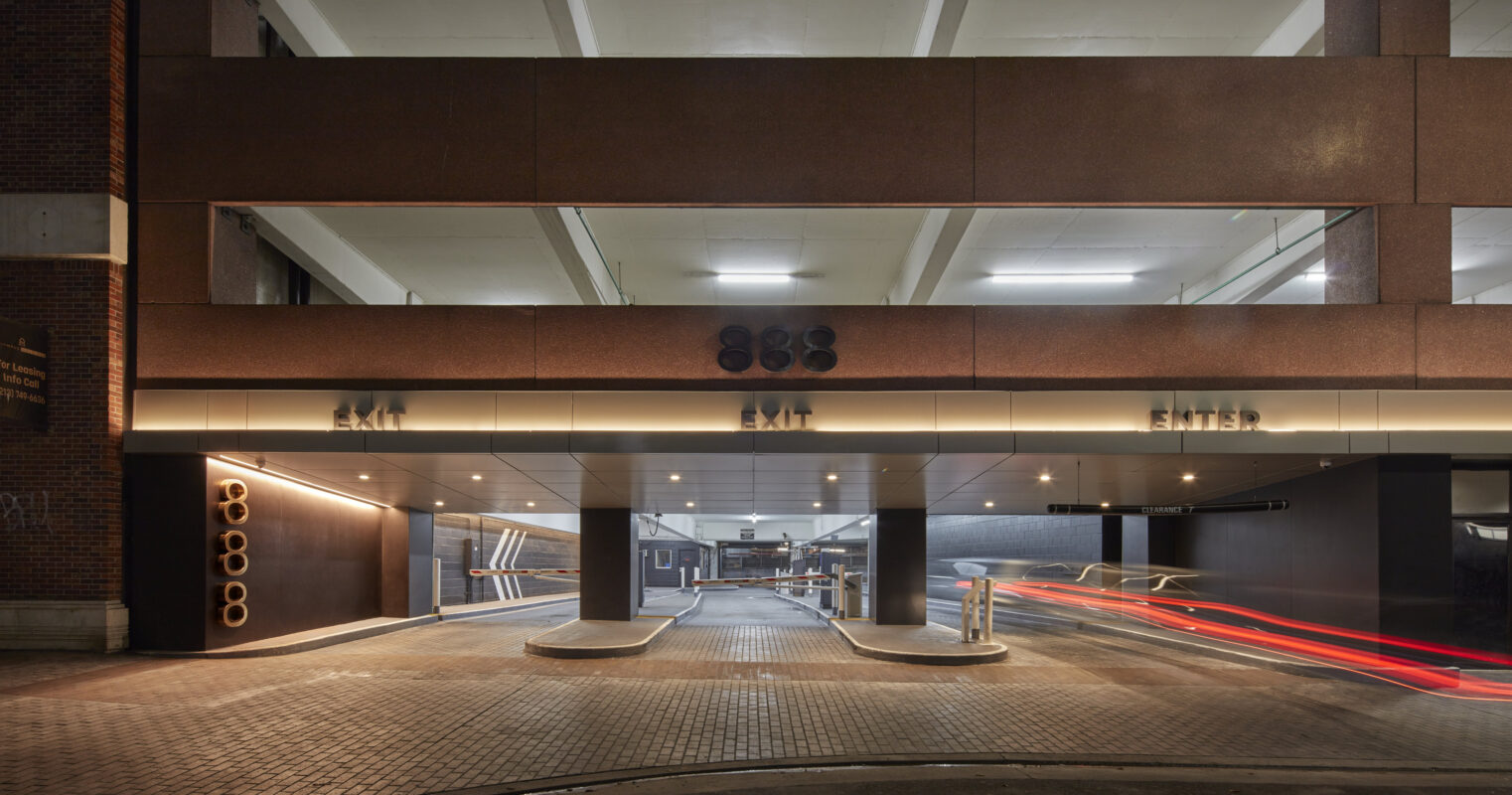 Modern parking structure featuring a sleek facade with a rich brown hue and illuminated signage for "ENTER" and "EXIT." The architectural design emphasizes functionality while integrating aesthetic elements such as recessed lighting and minimalist accents, enhancing both safety and visual appeal in urban settings.