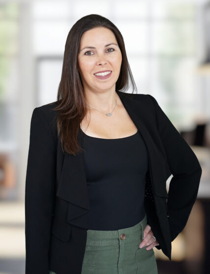 A professional woman standing confidently and smiling against an office background.