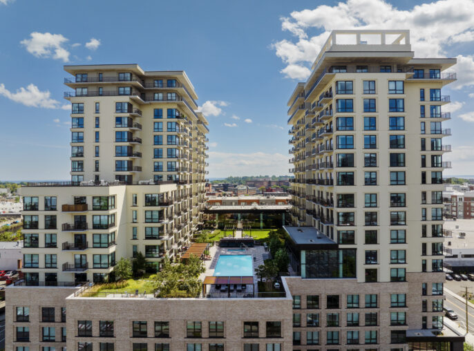 Aerial architectural view of 18 Dock Street in Stamford, Connecticut, showing two residential towers with balconies rising above a shared podium and landscaped central courtyard with outdoor swimming pool.